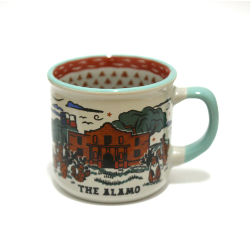 The Alamo Feeling Folky Mug is a ceramic mug with a light blue handle, featuring an illustrated Alamo scene with trees and cacti. "THE ALAMO" appears below the image, and the interior displays a bold red pattern.