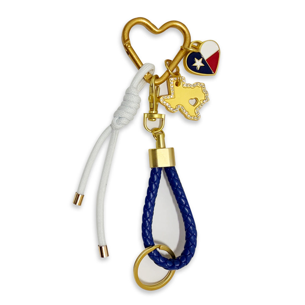 The Texas Carabiner Bag Clip features a gold heart-shaped carabiner holding three charms: a Texas flag heart, rhinestone-outlined Texas state, and a keyring with blue braided loop and white cord—ideal as an outdoor accessory or bag clip.