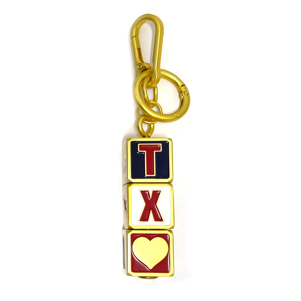 The Texas Block Spinner Bag Clip is a playful gold keychain with three stacked blocks: a red T on navy, a red X on white, and a yellow heart on white—perfect as a Texas accessory or gift.