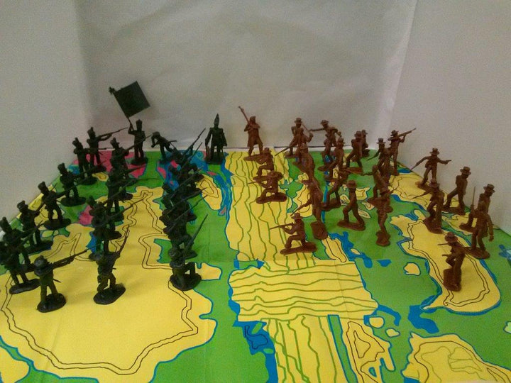 Alamo Toy Soldiers in green and brown PVC are arranged on a colorful map, some standing, kneeling, or holding a flag, positioned as if preparing for battle.