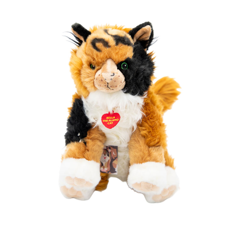 Bella the Cat Plush w/Collar features soft orange, black, and white fur, green eyes, a pink nose, and a red heart tag that says "Bella the Cat." It's a delightful Texas souvenir against a white background.