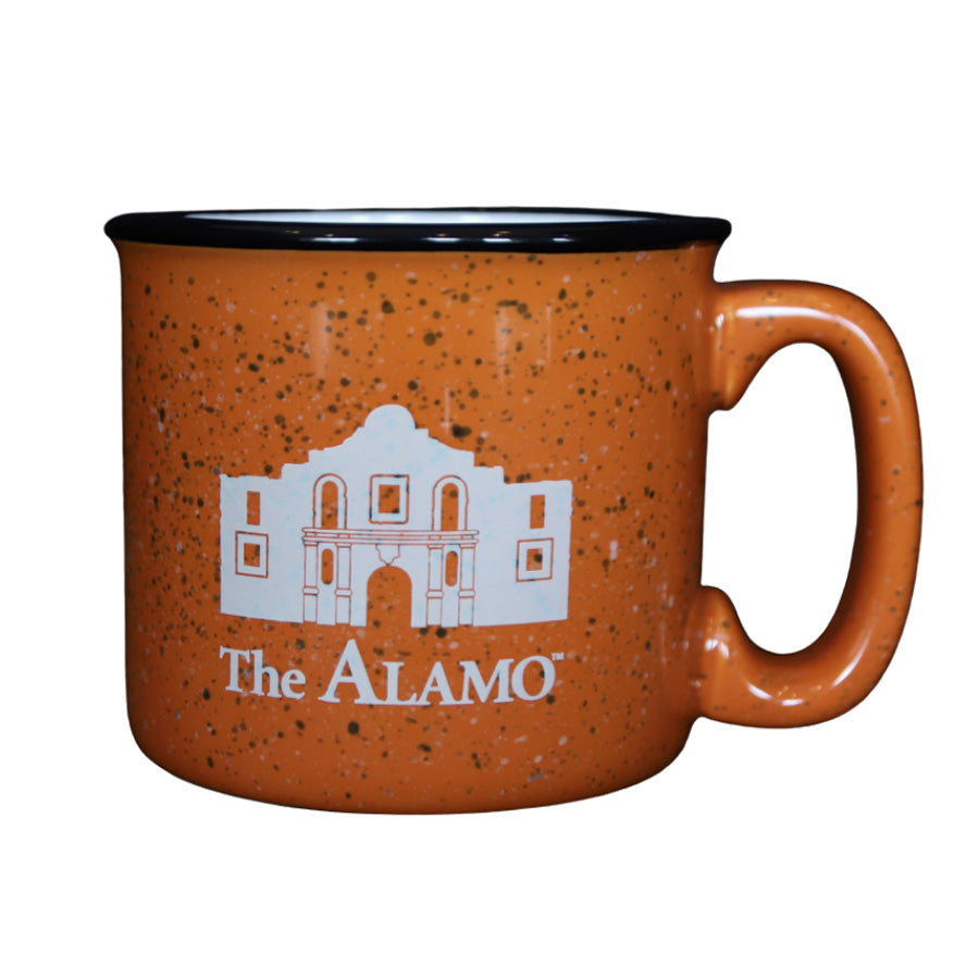 The Alamo Orange Mug is a speckled orange terracotta ceramic mug with a black rim, featuring a white illustration of the Alamo and "The ALAMO" text on the front.