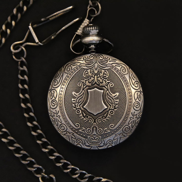 The Pocket Watch features intricate silver engravings, a decorative shield design on the cover, precise quartz movement, and comes attached to a metal chain, displayed against a black background.