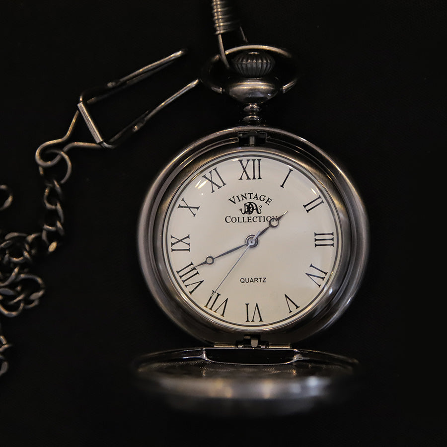 The Pocket Watch, with quartz movement, features a silver case, white face, black Roman numerals showing 10:09:36, an attached metal chain, and is displayed against a black background.