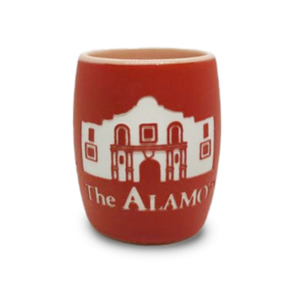 The Alamo Building Etched Shot Glass is a red ceramic keepsake featuring a delicate white illustration of the Alamo Building and the words “The Alamo” etched onto its surface, beautifully displayed against a clean white background.